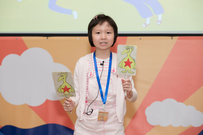 初小組決賽参賽者黎穎欣小朋友雙手拿著兩個黃色的紙偶講故事。